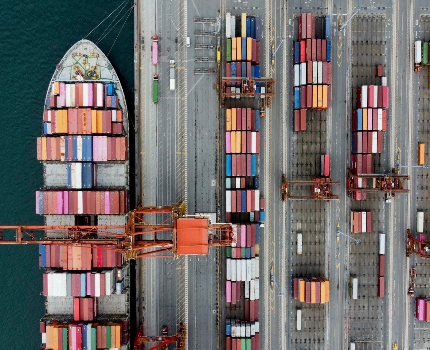Navio porta-contêineres atracado ao lado do pátio de contêineres de um terminal portuário, visto do alto